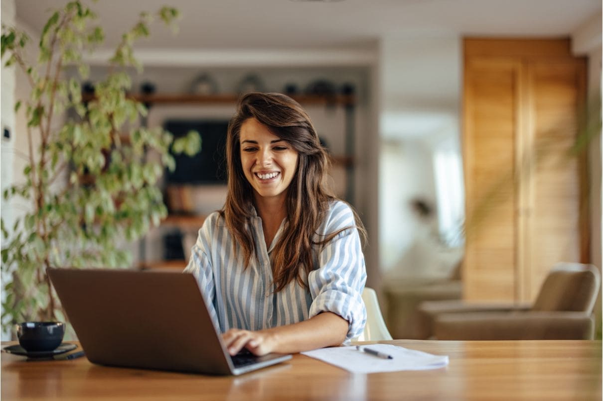A woman happily using her laptop, displaying a bright smile as she engages with the device's screen.